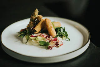 Panierte Gemüsesticks auf einem frischen Salatbett mit Radieschen und Blättern auf weißem Teller.