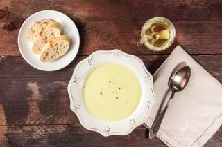 Cremige Suppe mit Pfefferkörnern in dekorativer Schale, serviert mit Baguettescheiben und Weißwein.