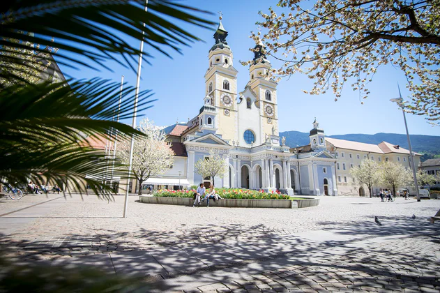 Dwie osoby siedzą w centrum Brixen. Z tyłu widać katedrę.