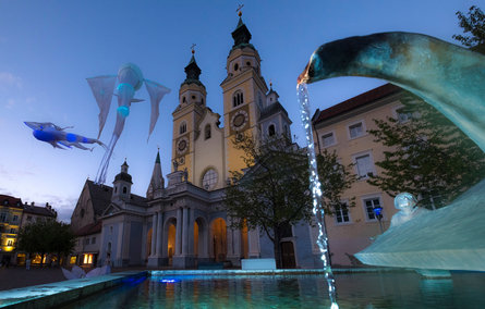 Veduta di creature marine luminose e fluttuanti sopra la piazza del Duomo di Bressanone al Lightfestival Bressanone