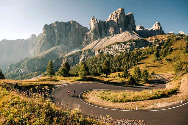 Dva cyklisté na silničních kolech jedou za krásného počasí serpentinami v oblasti Alta Badia Dolomity.