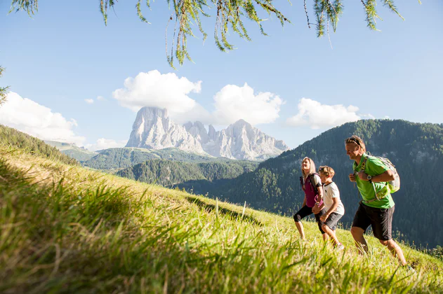A family of three enjoys a mountain hike in the Dolomites region Val Gardena during a sunny summer day