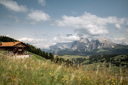 A group of people sitting at the tables of a mountain hut during a summer day in the Dolomites region Seiser Alm