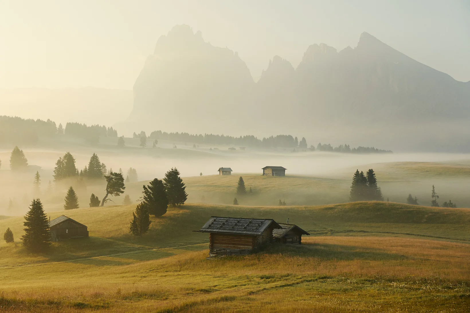 Malghe di montagna immerse nella leggera nebbia mattutina di una giornata estiva in Alto Adige