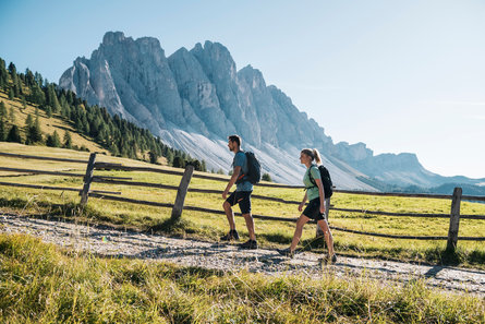Due persone camminano lungo un sentiero in Val di Funes con le Odle sullo sfondo