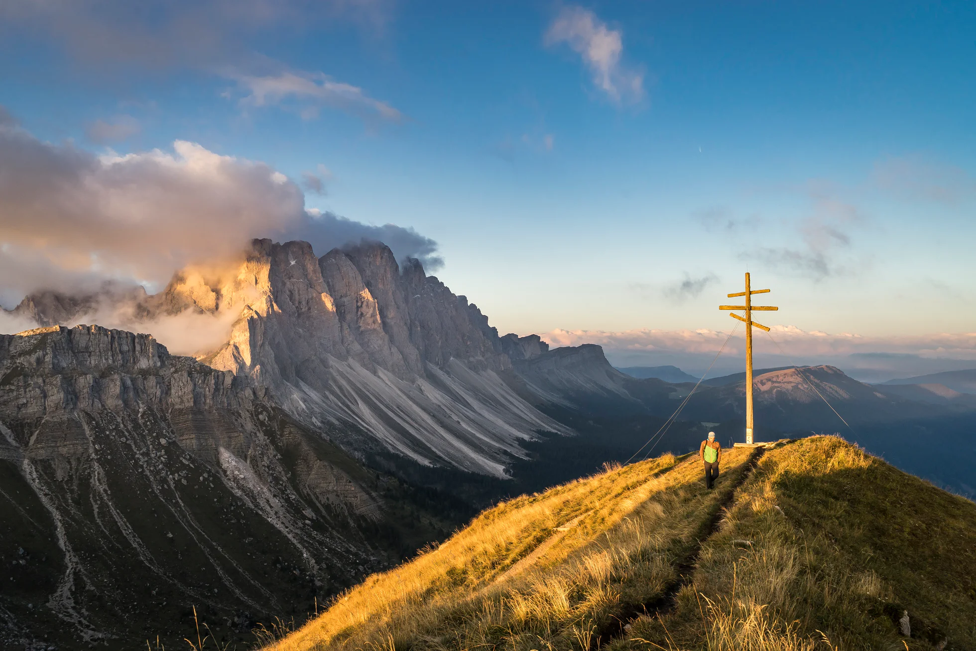 A man stands on a mountain with a mountain range in the background in the Dolomites Region Villnösstal