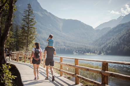 A family with a child walking along the lake in the Antholzertal valley. The father is carrying the son on his shoulders.