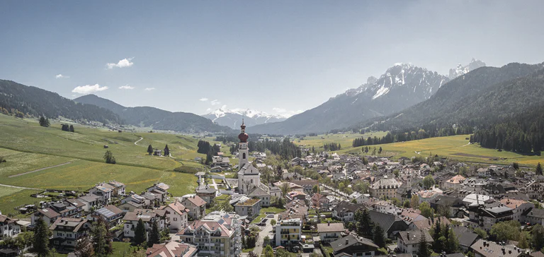 Vista sul paese di Villabassa con il grazioso campanile della chiesa al centro. Sullo sfondo un paesaggio boschivo e imponenti montagne