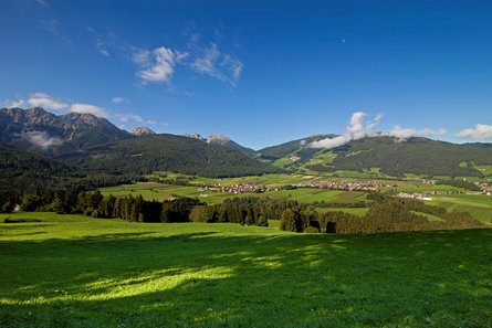 Vista sul paese di Valdaora tra prati verdi e pendii boschivi in estate