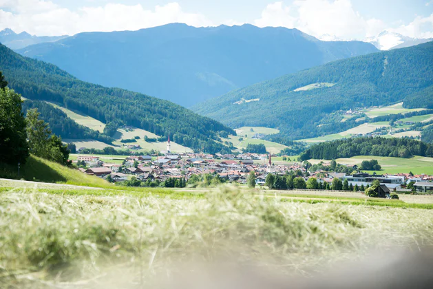 Olang in the middle of green fields and forests during a sunny summer day in the Kronplatz Dolomites region.