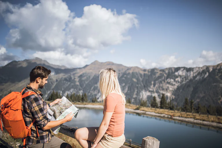 Una coppia seduta di fianco ad un laghetto di montagna studia una cartina geografica tascabile mentre ammira il panorama nei dintorni di Racines 