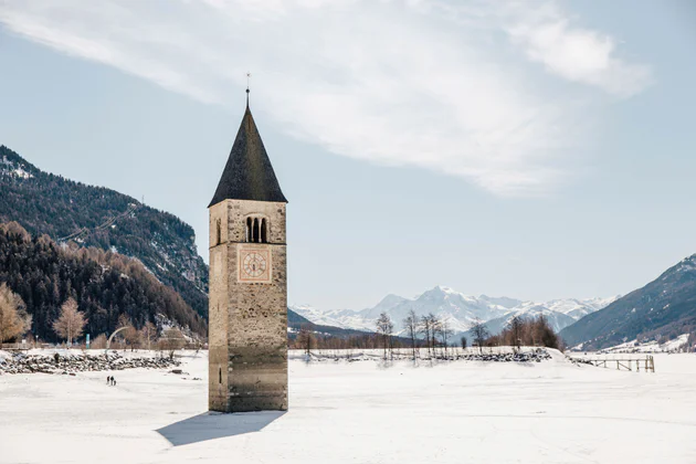 Vista sul lago di Resia con il campanile sommerso, sullo sfondo le cime innevate