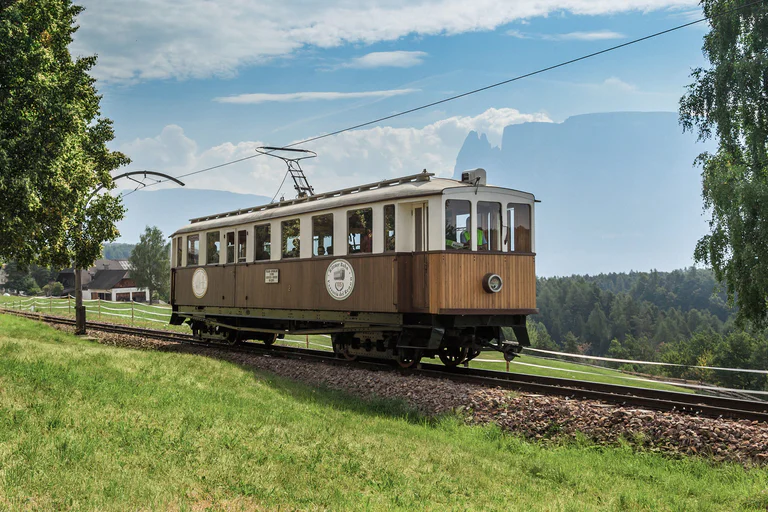 Lo storico treno del Renon in primo piano con panorama boschivo sullo sfondo
