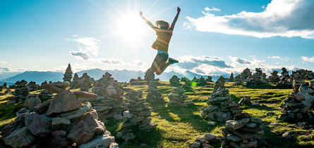In una bella giornata soleggiata una ragazza salta gioiosa sulla collina tra gli omini di pietra sopra la Val Sarentino