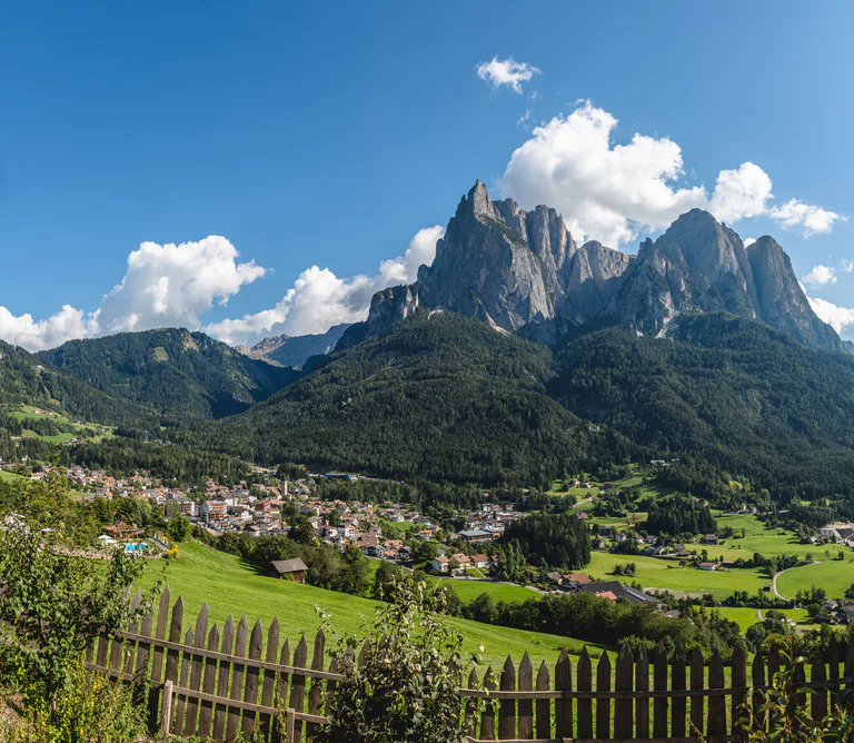 Vista sulla località Siusi allo Sciliar circondata da prati verdi, boschi e montagne dolomitiche