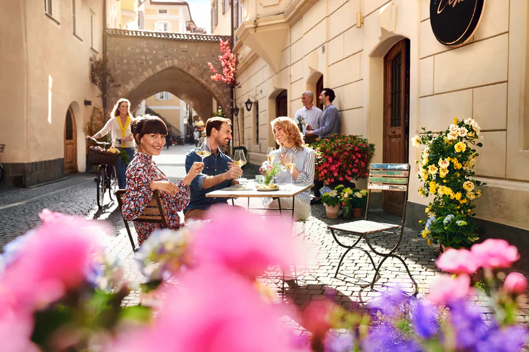 Dwie kobiety i dwóch mężczyzn z uśmiechem spożywa aperitif, siedząc pod gołym niebem na starówce Bolzano.