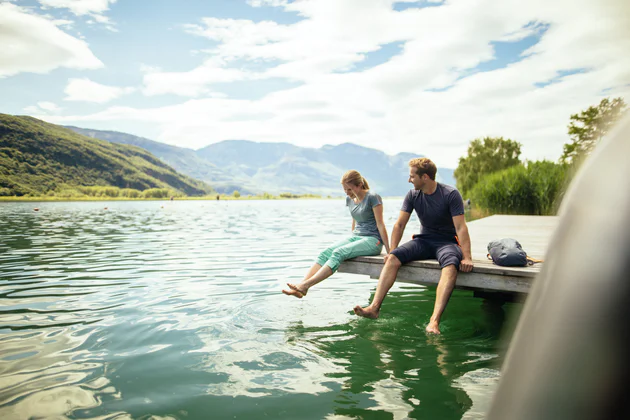 Zwei Personen sitzen an einem Steg und lassen die Füße im Wasser baumeln