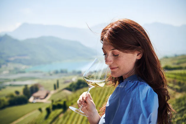Eine Frau genießt ein Glas Weißwein mit Blick auf den Kalterer See und die umliegenden Weinberge