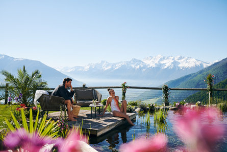 Due persone sedute a bordo piscina su una terrazza panoramica con vista sulla Val Venosta