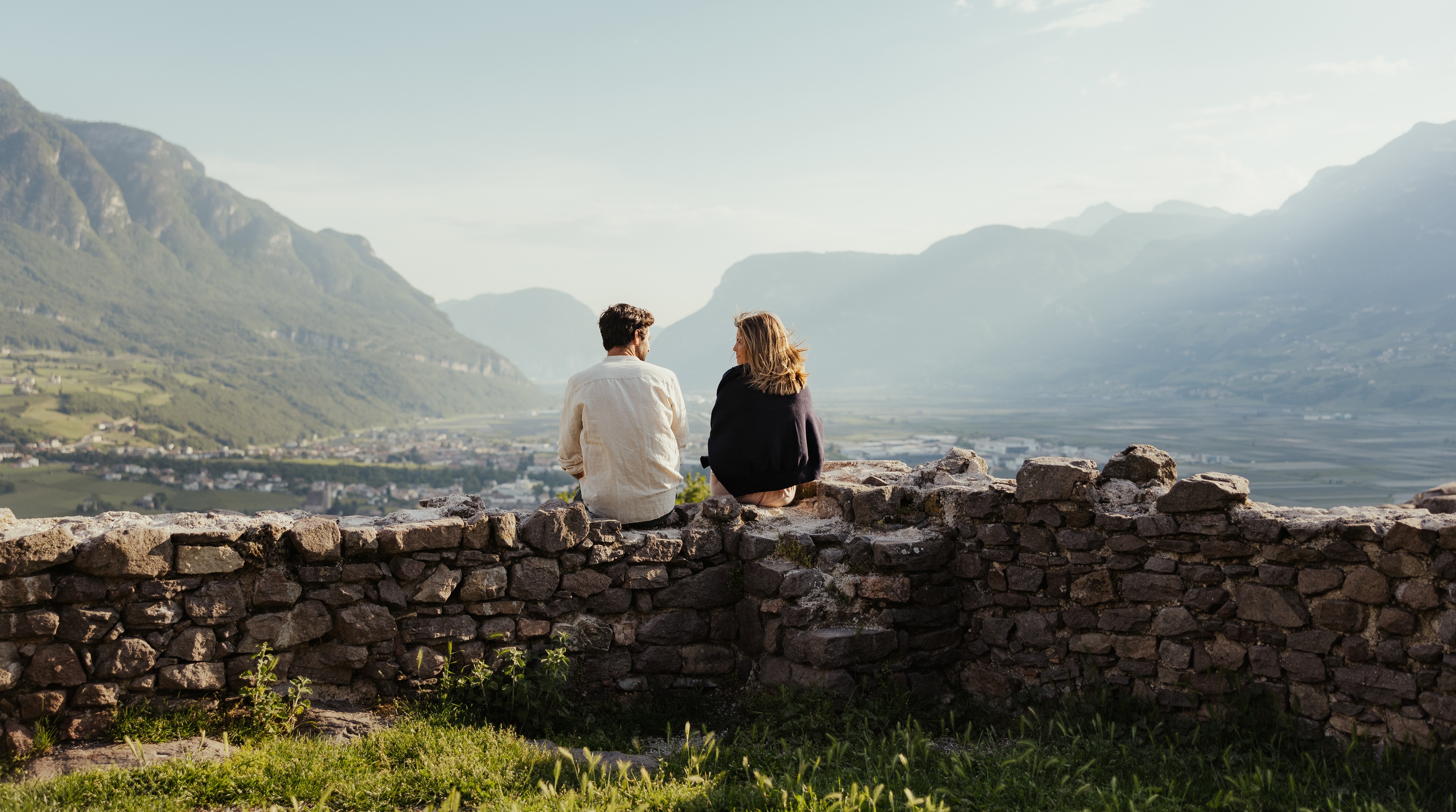 Una coppia seduta su un muro di pietra si gode il panorama della vallata da una collina