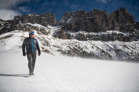Expert na sníh Georg Eisath kráčí po sněhové pokrývce před horským panoramatem.