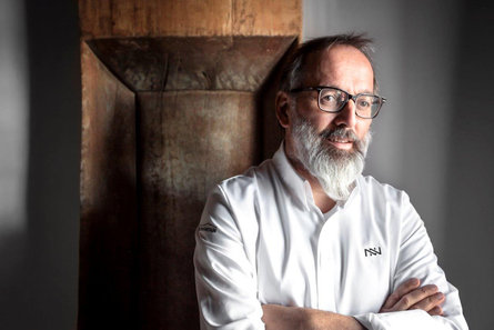 A portrait of chef Norbert Niederkofler wearing a shirt bearing his initials.