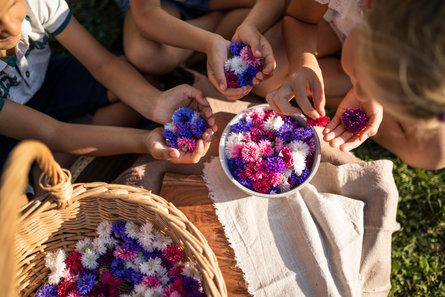 Drei Kinder sitzen um einen Korb voller Blumen