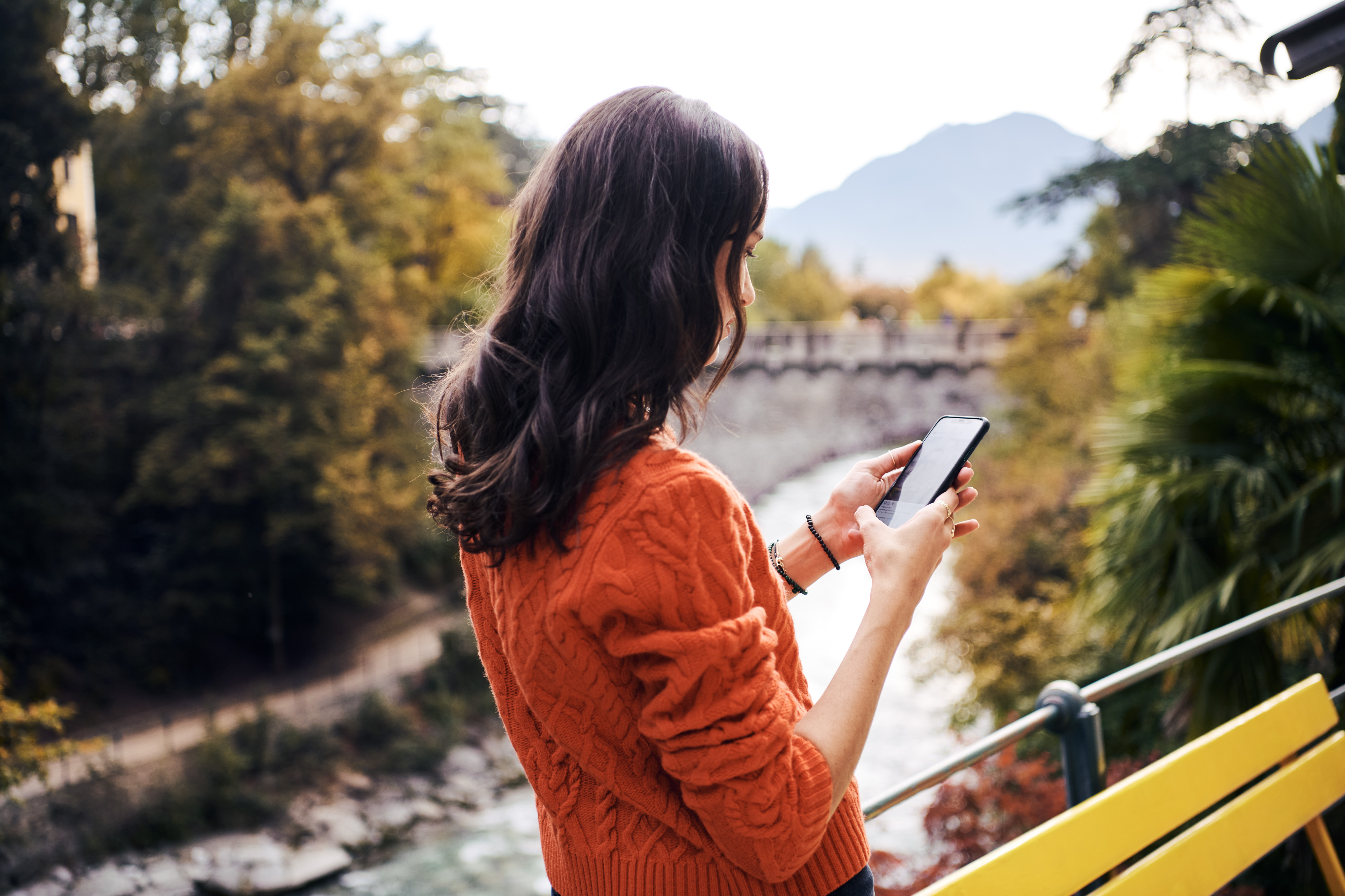 Eine Person mit einem Handy in der Hand und Meran im Hintergrund