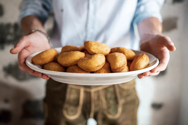 Een man heeft een bord met Canci Checi in de hand: traditionele Ladinische, gefrituurde Schlutzkrapfen.