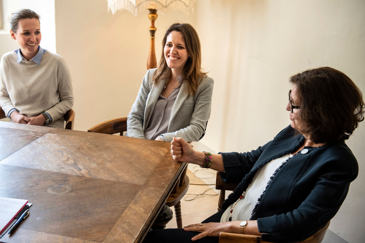 Winzerin Elena Walch (rechts) sitzt mit ihren Töchtern Karoline und Julia (von links) im Gespräch an einem alten Holztisch.