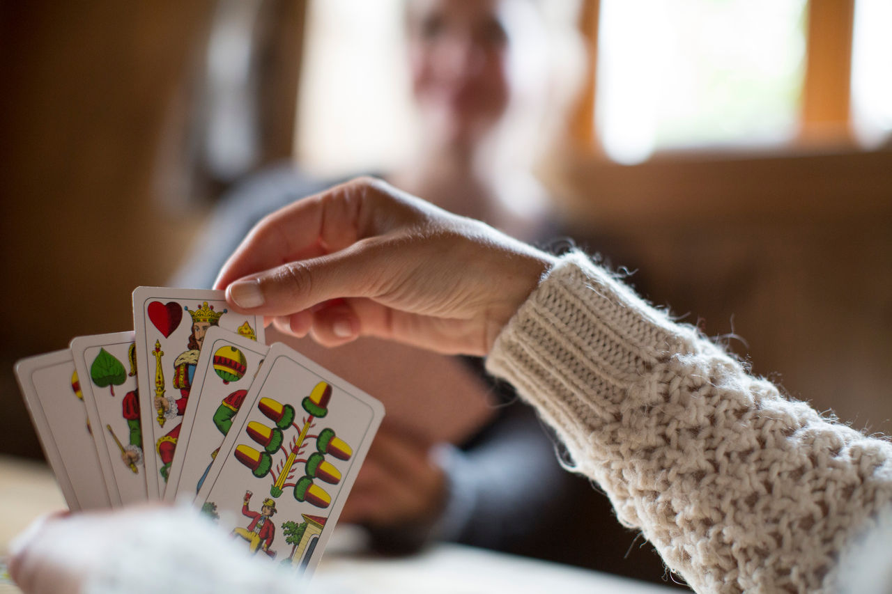 Eine Frau hält fünf Karten des Südtiroler Kartenspiels Watten in ihrer linken Hand und zieht eine der Karten mit der rechten Hand.