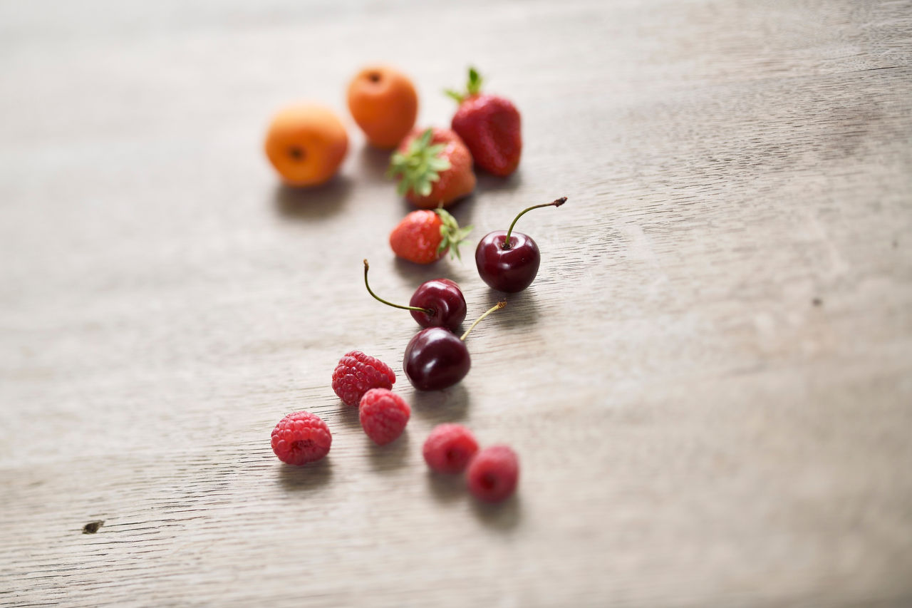 Aprikosen, Erdbeeren, Kirschen und Himbeeren aus Südtirol liegen auf einem Holztisch.