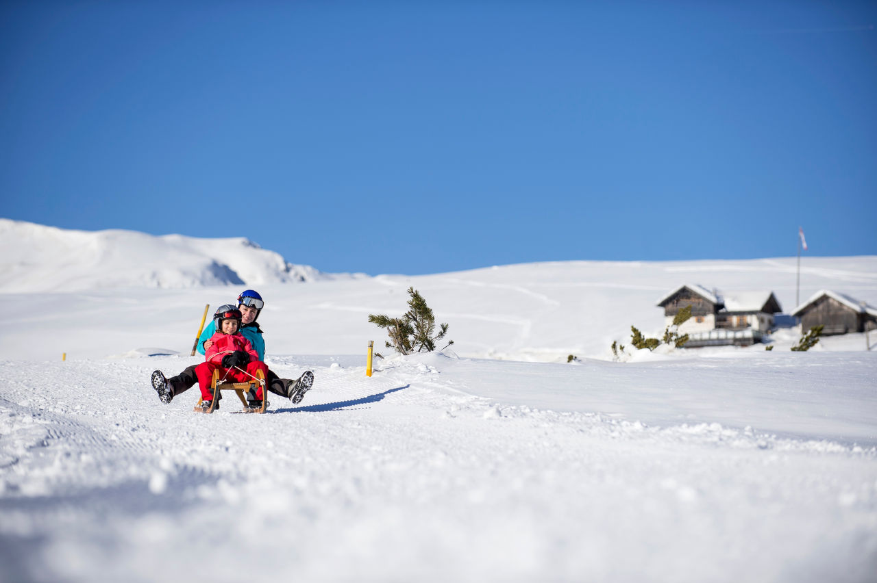 Eine Frau und ein Kind rodeln auf einem Schlitten auf der Villanderer Alm.