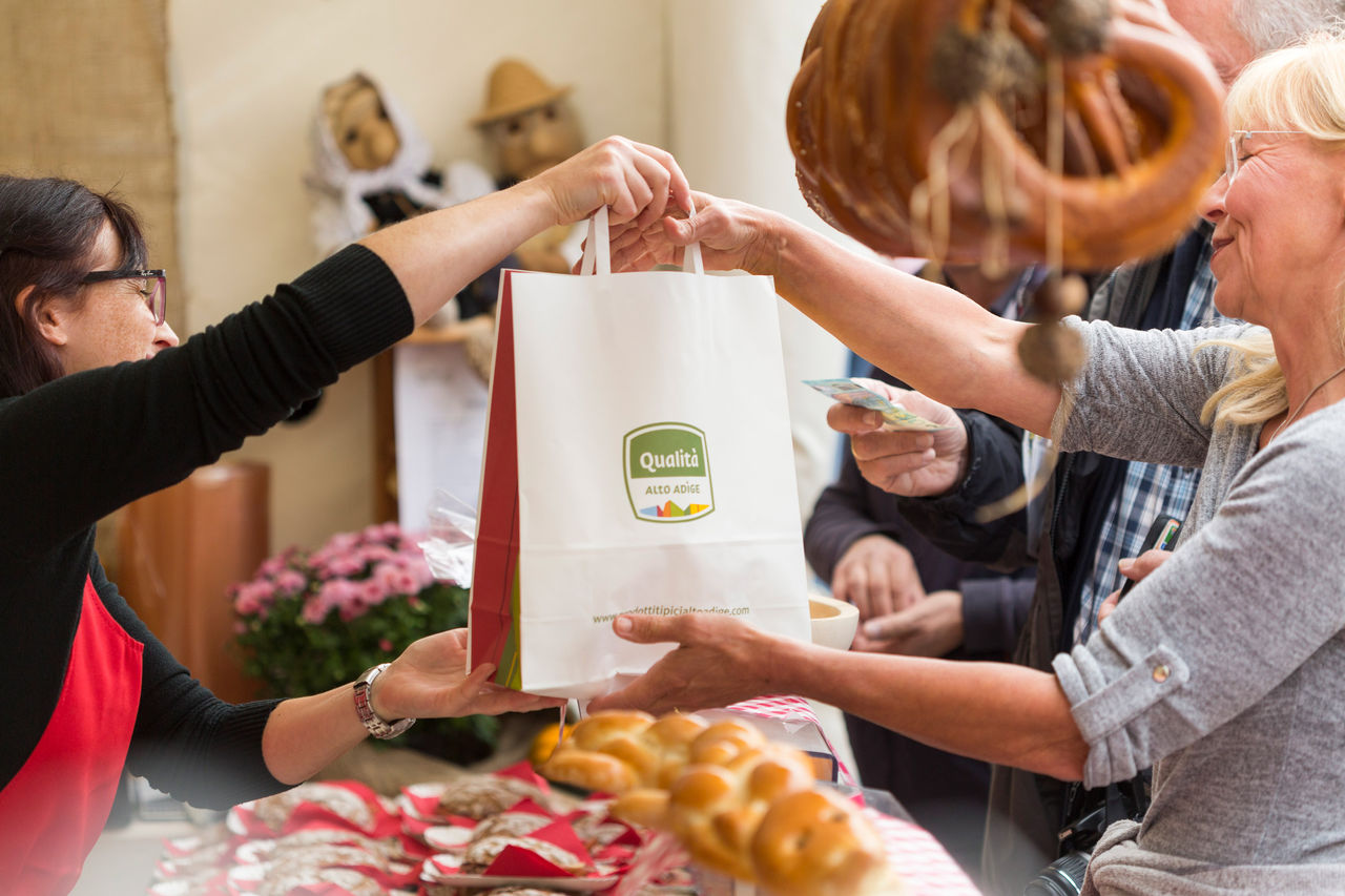 Zwei Personen lassen sich von einem Händler Obst auf dem Obstmarkt zeigen