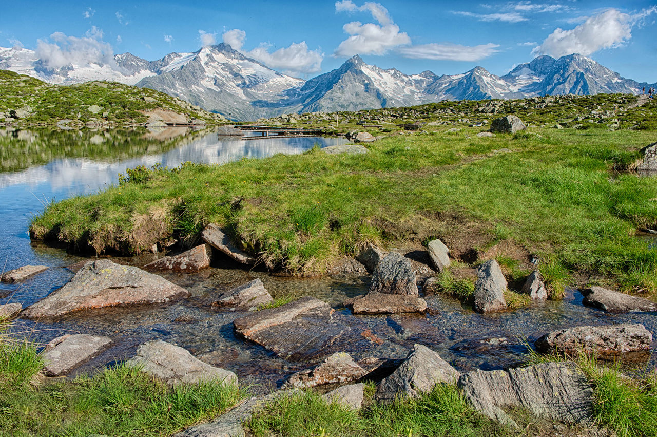 Ein Bach schlängelt sich durch eine Wiese des Ahrntals in der Nähe des Klausbergs.