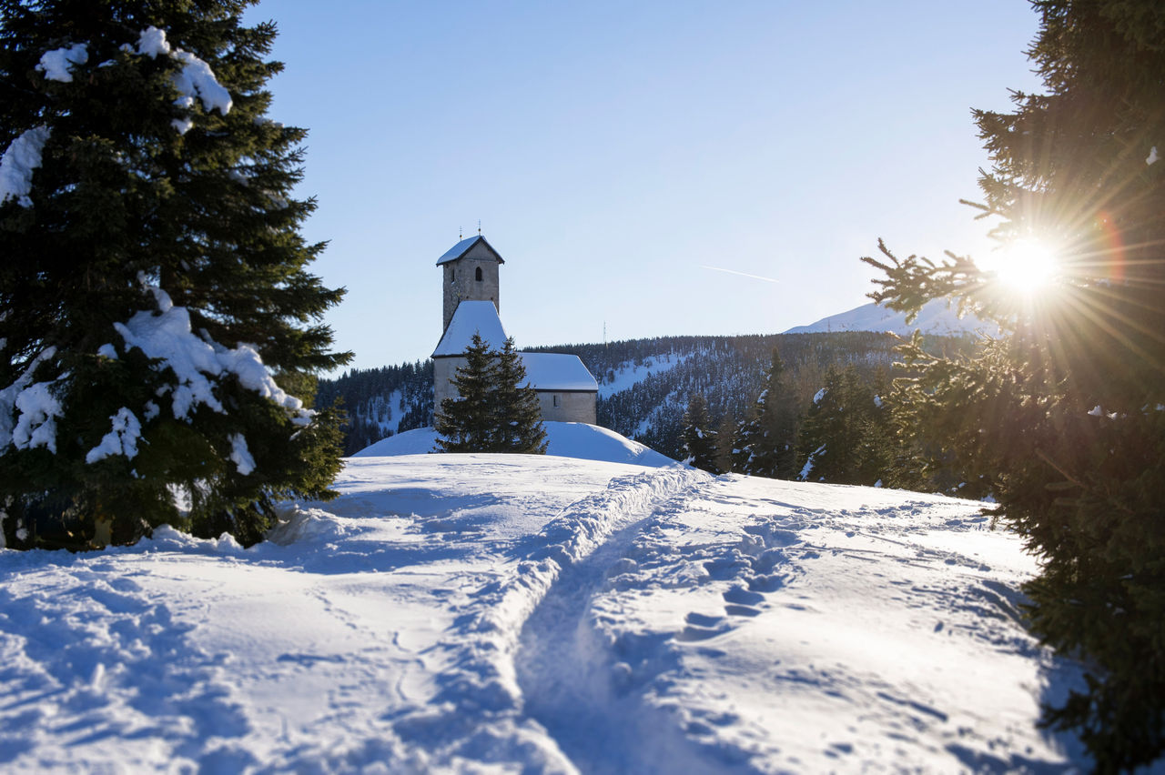 Die Sonne scheint auf eine Kirche im schneebededeckten Naturschutzgebiet Vigiljoch.