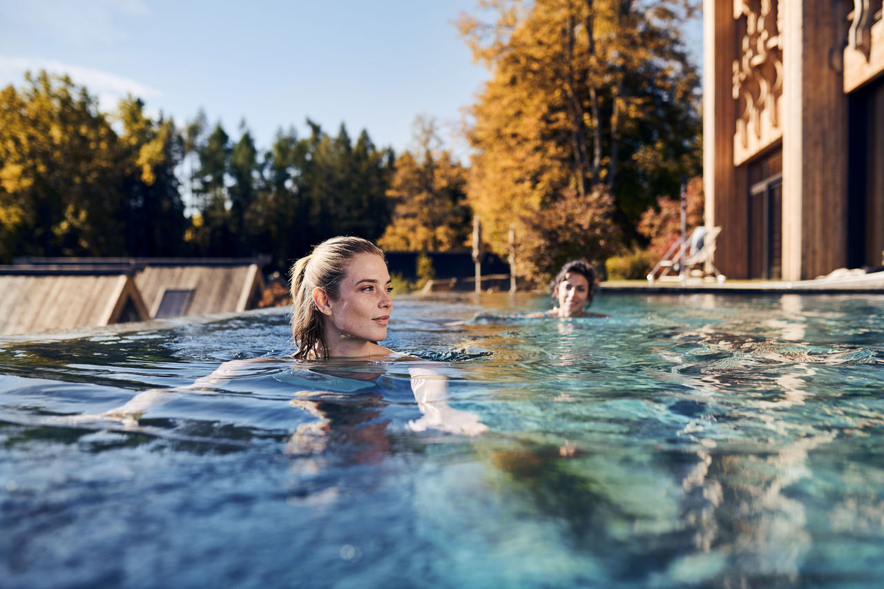 Zwei Damen schwimmen im Pool mit Blick auf goldgefärbte Lärchen