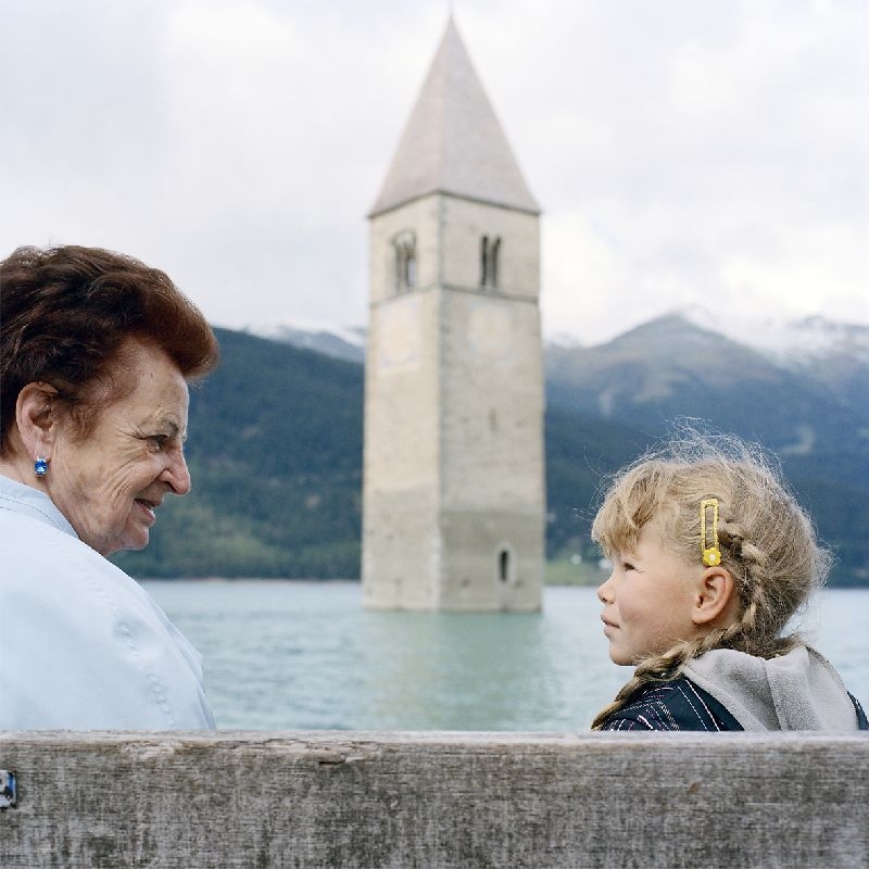 Theresa Theiner und ihre Enkelin sitzen am Reschensee mit dem Kirchturm im Hintergrund