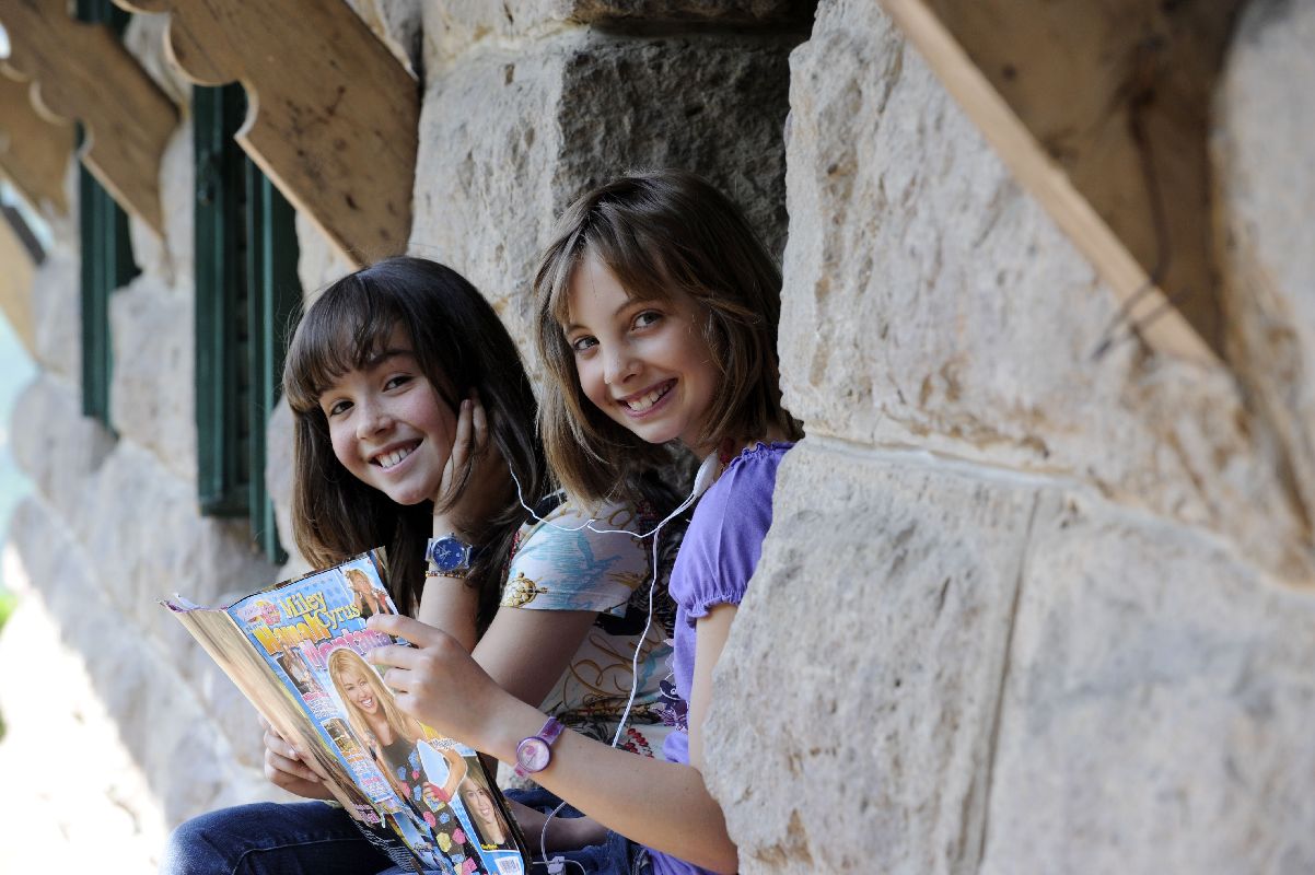 Zwei Mädchen lächeln in die Kamera, hören dabei Musik und halten ein Jugendmagazin in den Händen.