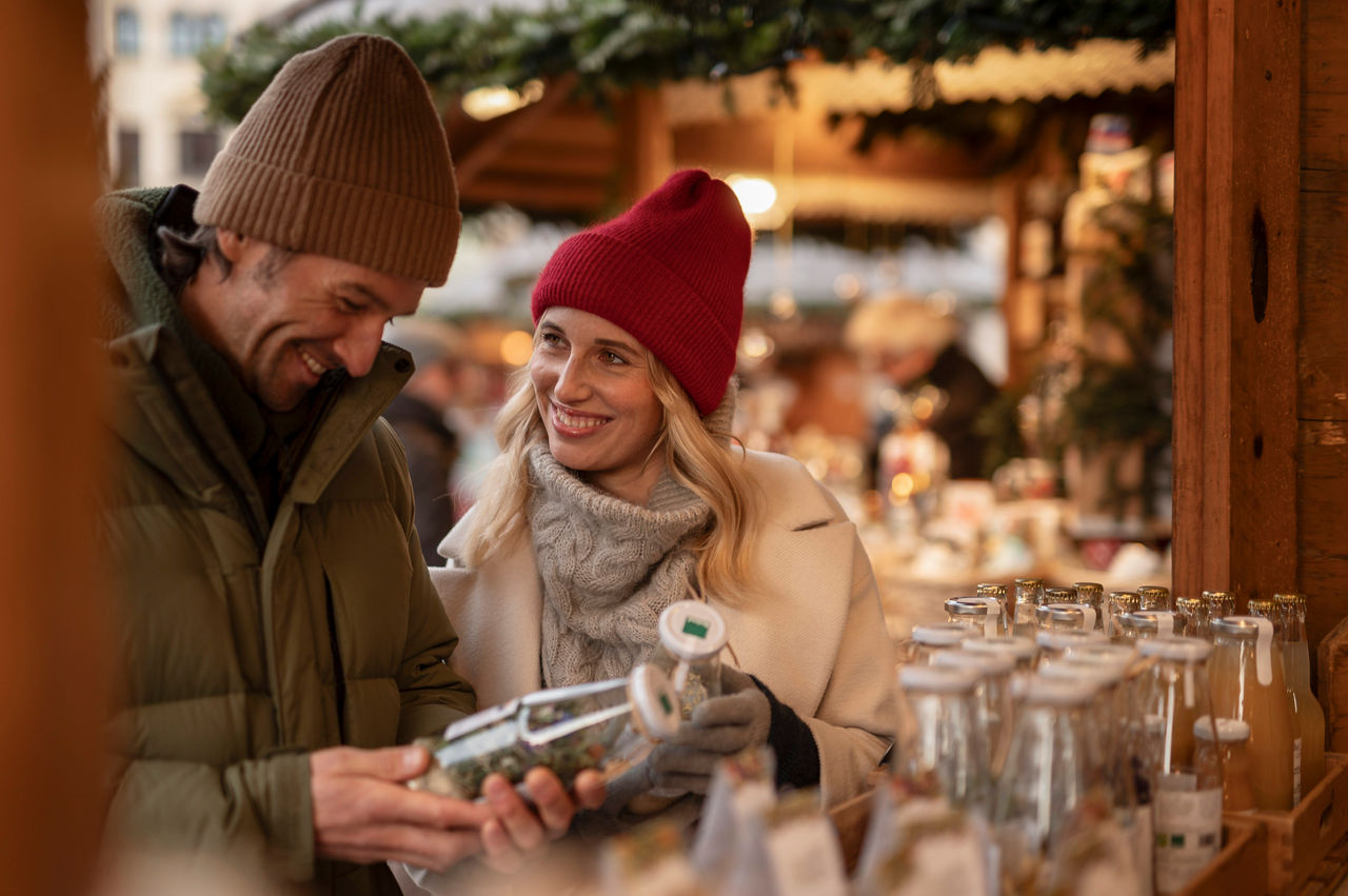 Zwei Menschen stehen an einem Stand auf dem Weihnachtsmarkt und sehen sich die Produkte an