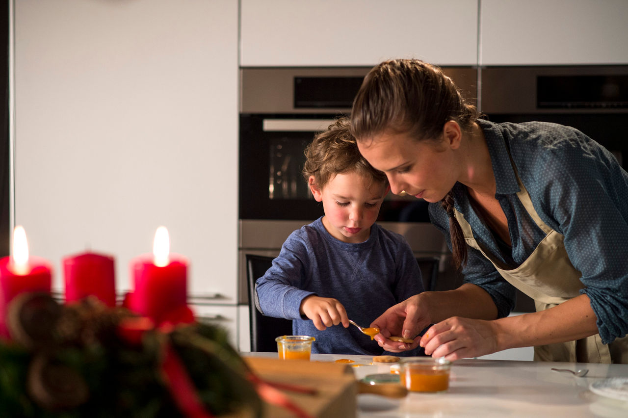 Eine Mutter backt mit ihrem Sohn Weihnachtskekse mit Konfitüre. 