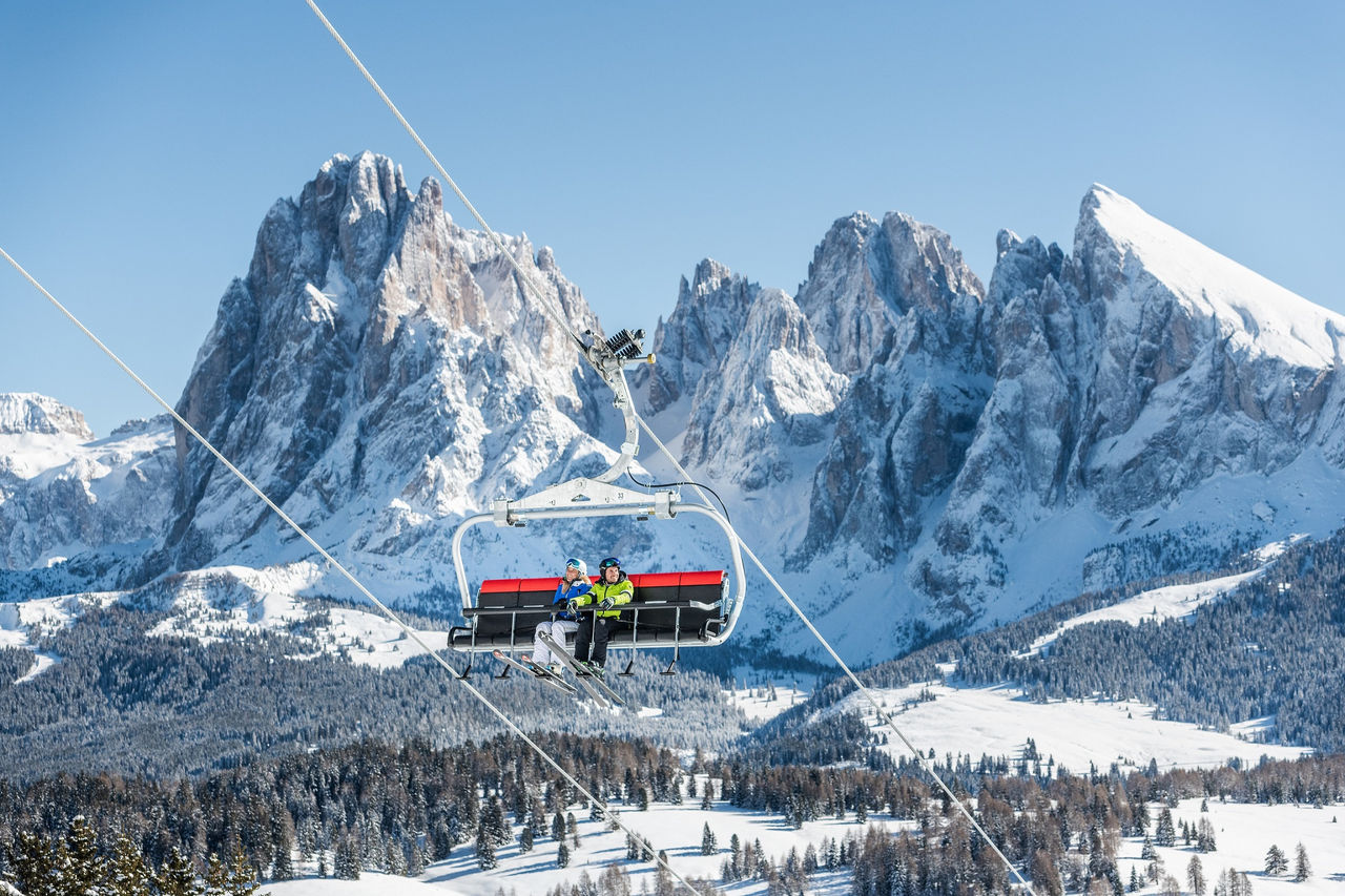Eine Skifahrerin und eine Skifahrerin sitzen im Sessellift auf dem Weg zur Skipiste auf der Seiser Alm.