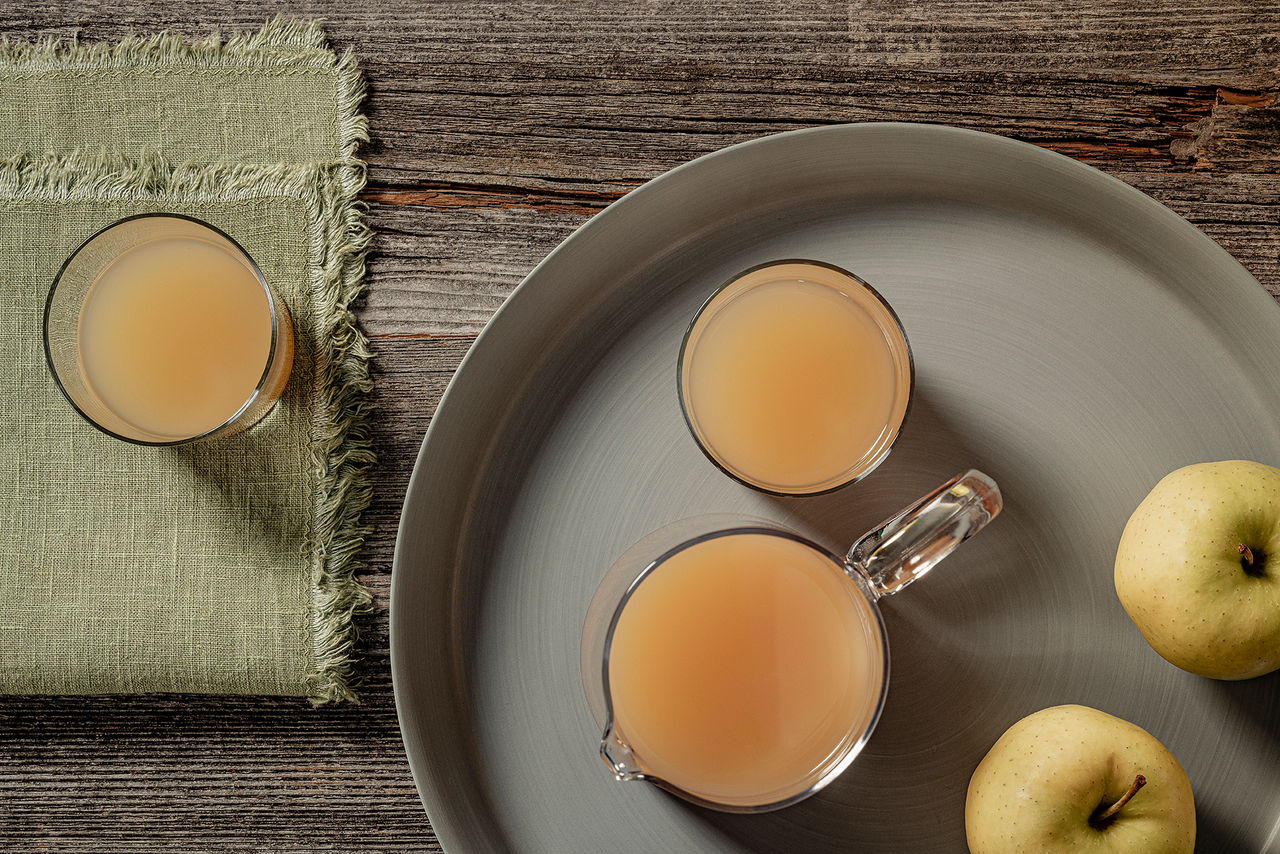 Drei gläser Naturtrüber Apfelsaft aus Südtirol stehen auf einem Tisch daneben liegen zwei Äpfel