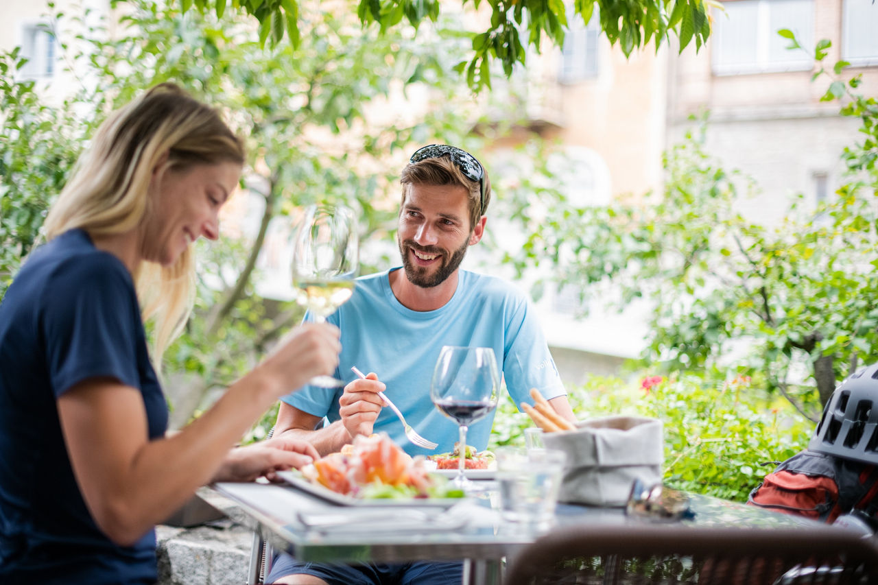 Zwei Personen sitzen an einem Tisch im Freien und genießen leichte Sommergerichte und ein Glas Wein in Bruneck