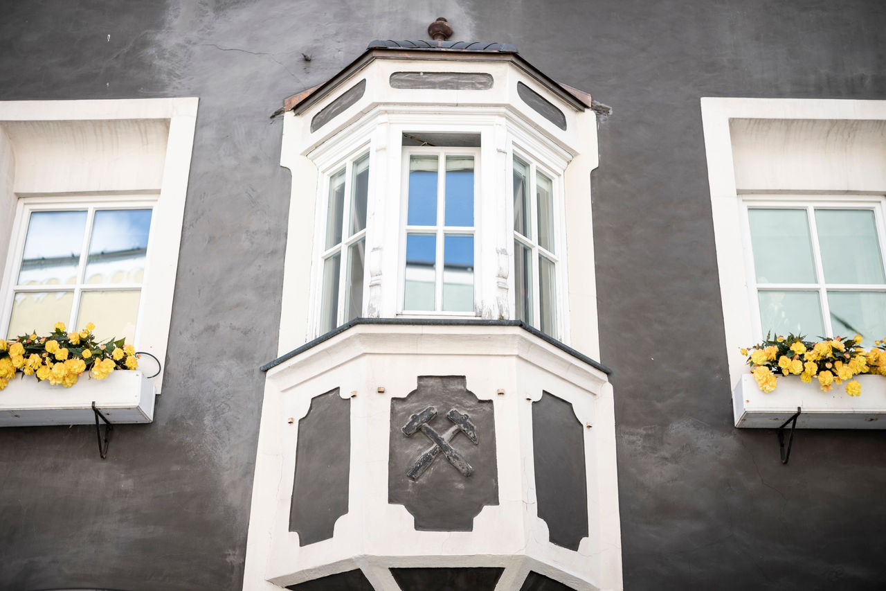 Mittelalterlicher Erker mit Bergbau-Emblem und blumengeschmückten Fenstern auf beiden Seiten