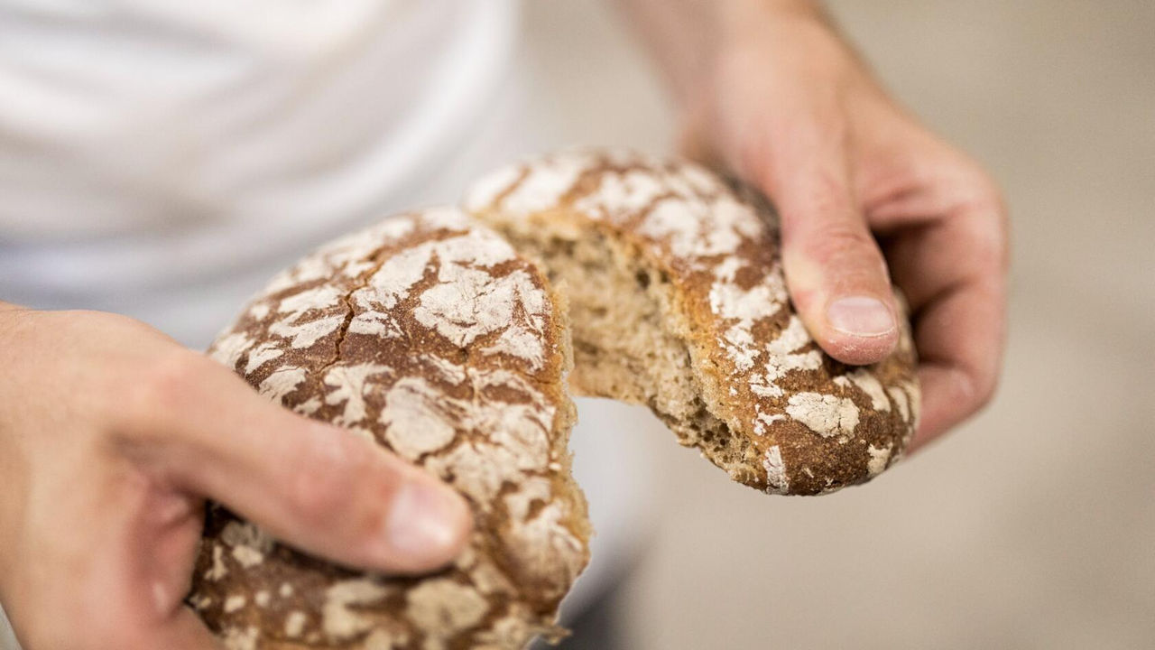 Eine Person teilt einen Laib SÃ¼dtiroler Brot in zwei