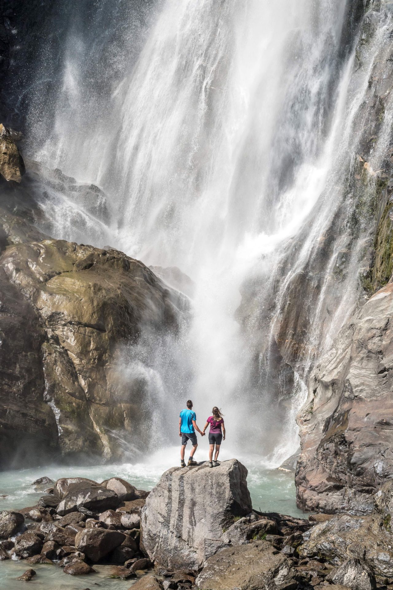 Zwei Person stehen vor einem Wasserfall und bestaunen das Naturschauspiel