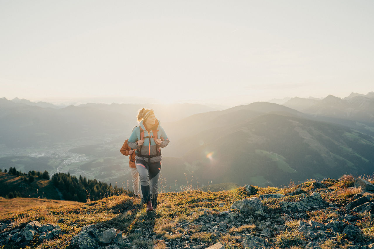 Zwei Personen wandern durch das Eisacktal mit der Sonne im Hintergrund