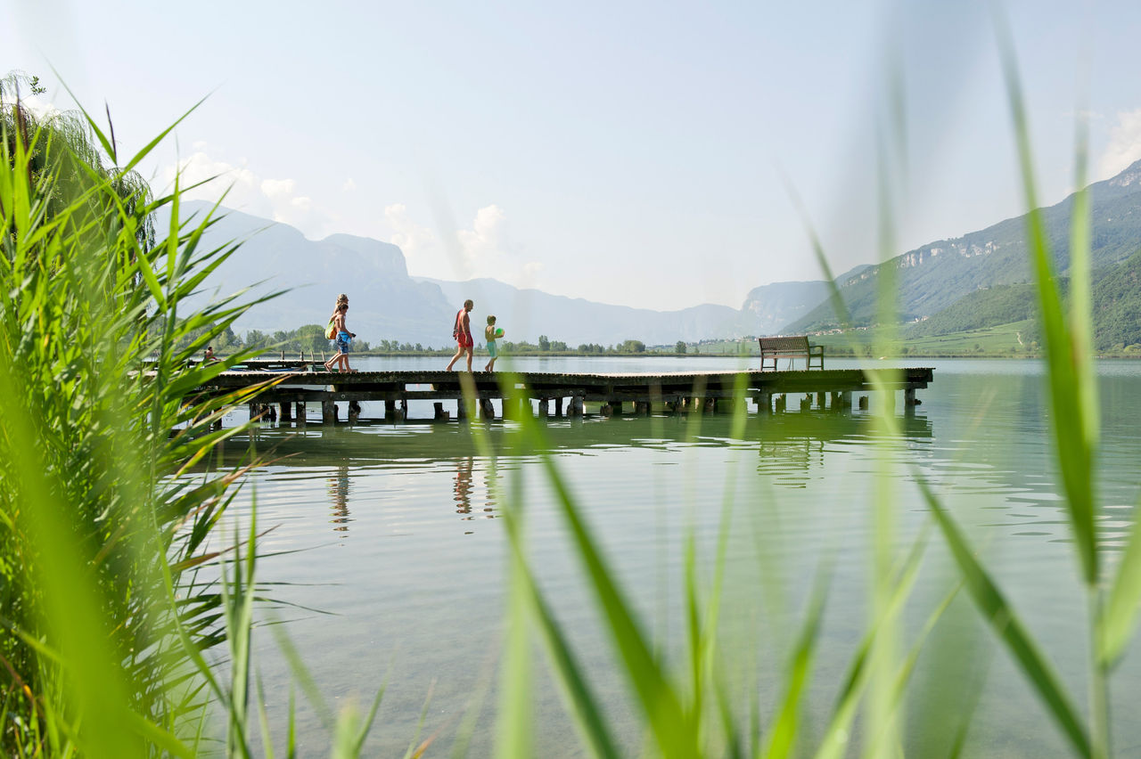 Eine Familie läuft über einen Steg am Kalterer See zum schwimmen