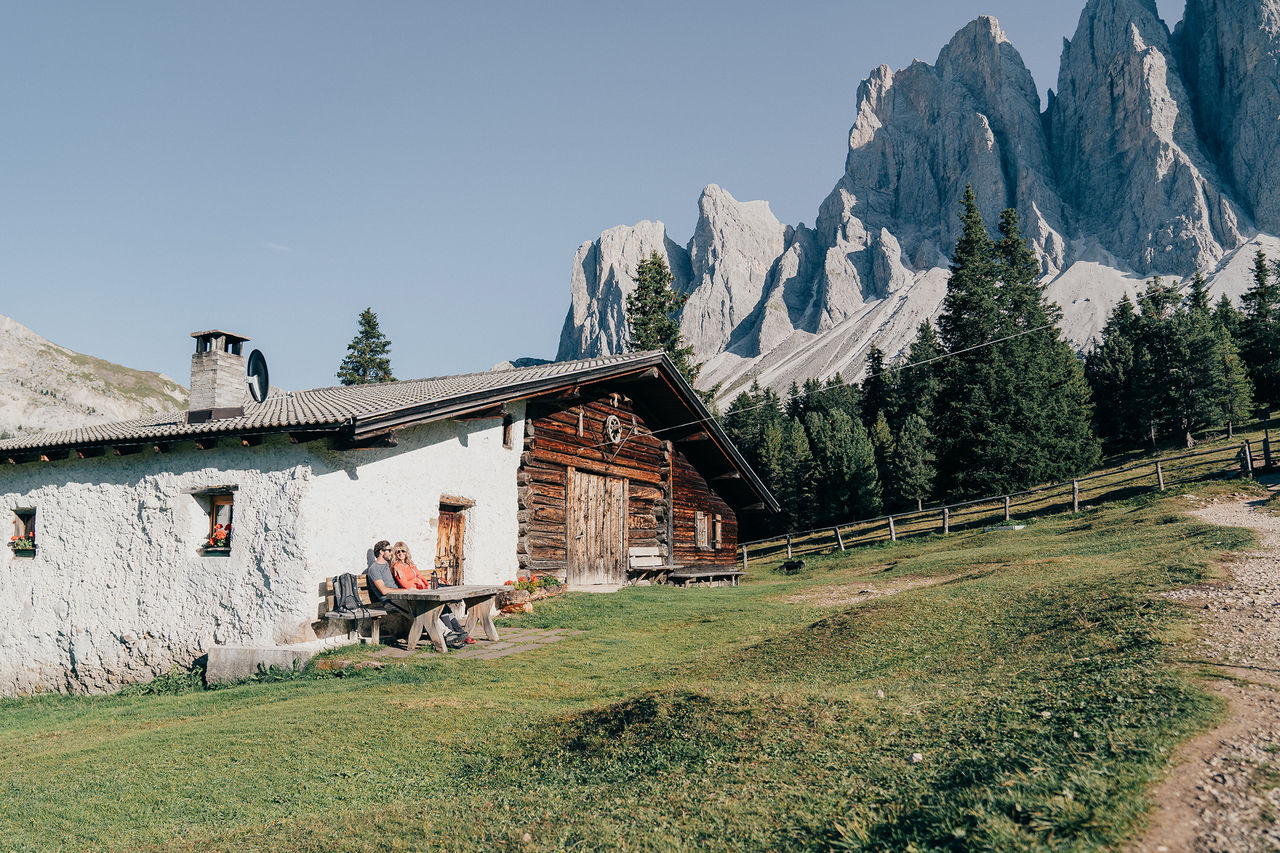 Zwei Personen sitzen vor einer Hütte am Villnösser Geisler